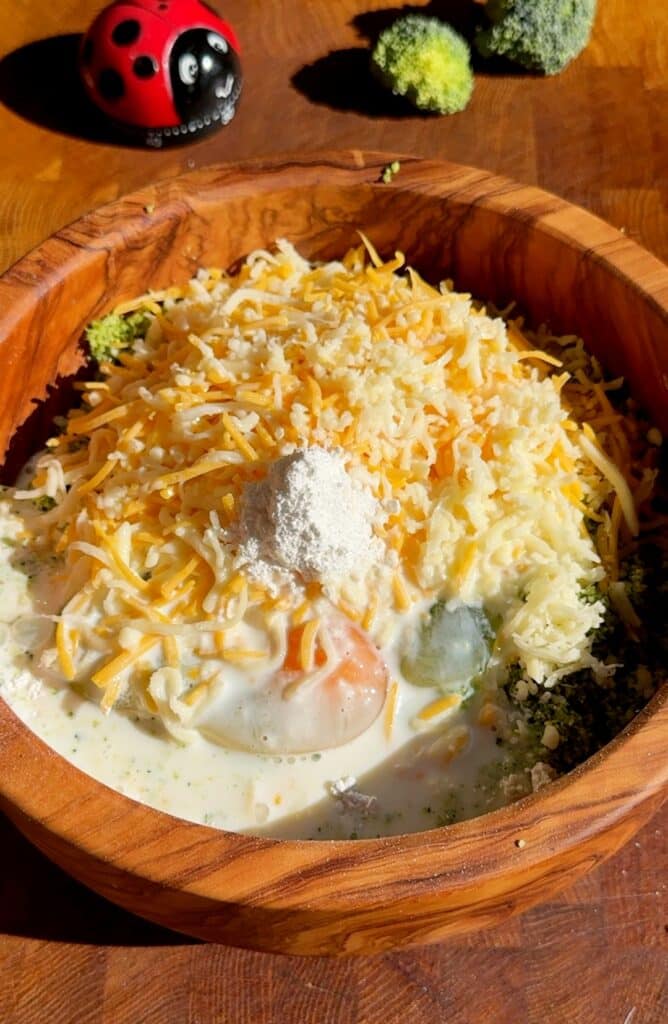 In a large mixing bowl, add the flour, grated broccoli, eggs, shredded cheddar cheese, salt, baking powder, baking soda, and milk.