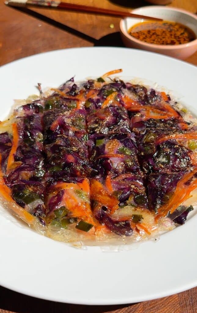 Crispy golden rice paper pancakes filled with colorful vegetables, served with tangy dipping sauce on a white plate