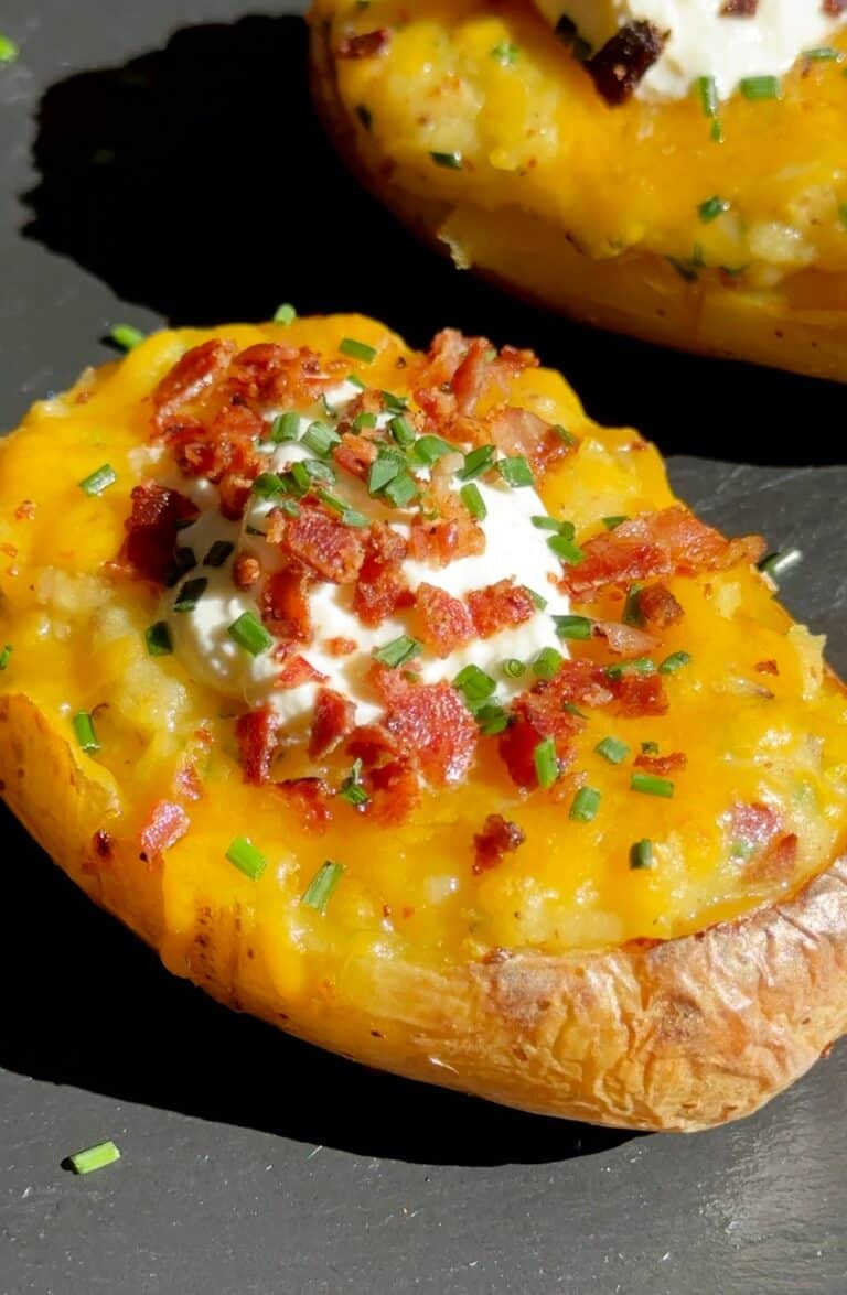 Cheesy Twice Baked Potatoes on a serving plate, golden and crispy on top, filled with creamy potato, cheese, bacon, and garnished with chives and sour cream.