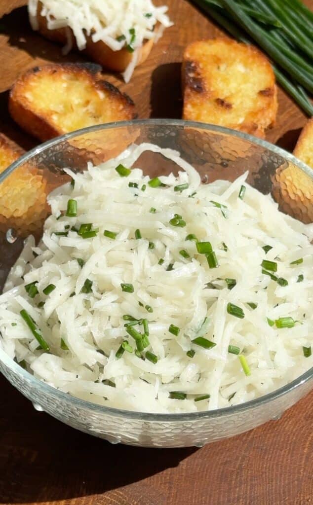Bowl of fresh German daikon radish salad with julienned radish and chopped chives, served with golden toasted baguette slices on the side.