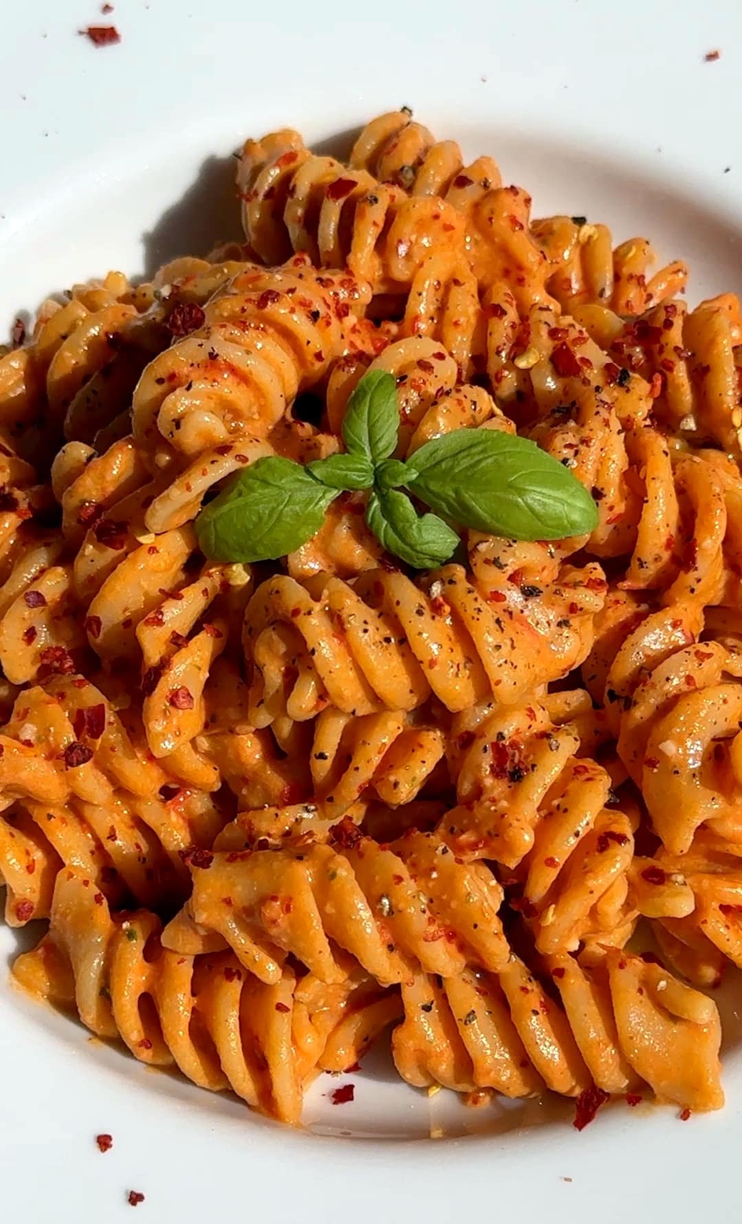 Creamy tomato burrata pasta plated, drizzled with olive oil, sprinkled with chili flakes, and garnished with fresh basil leaves, ready to serve.