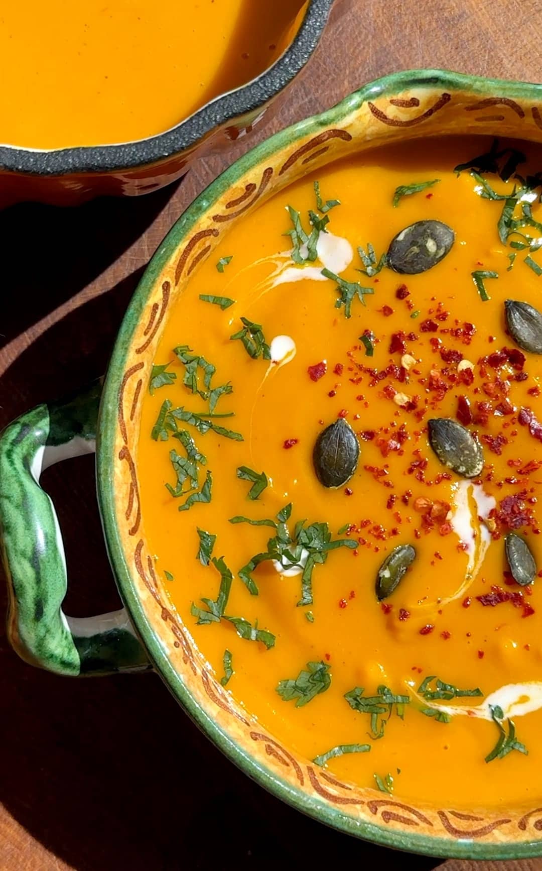 Creamy roasted squash and sweet potato soup served in bowls, garnished with pumpkin seeds, chili flakes, and fresh parsley.