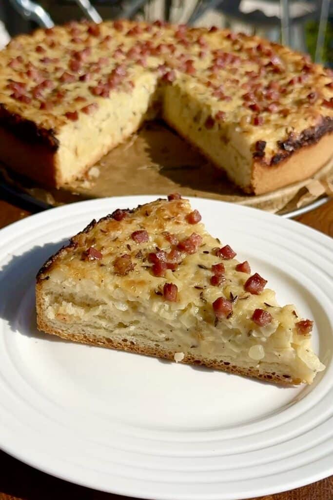 Close-up of a slice of German Onion Pie (Zwiebelkuchen) with golden crust, creamy onion filling, and bits of smoked bacon on top, served on a plate.