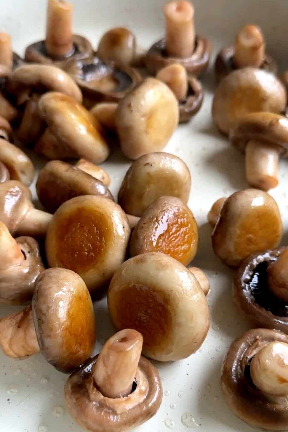 Whole mushrooms sizzling in hot sunflower oil in a large skillet, browning evenly as they cook undisturbed.
