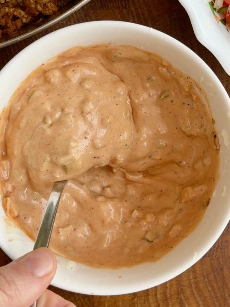 Creamy taco sauce made with mayonnaise, ketchup, mustard, diced onion, pickle, and smoked paprika in a bowl