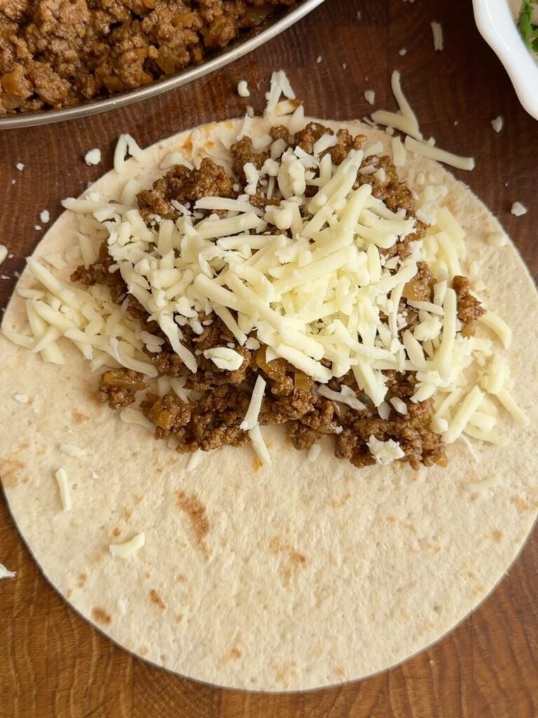 Tortilla layered with Gouda cheese and seasoned beef, folded and ready to be cooked until golden and crispy.