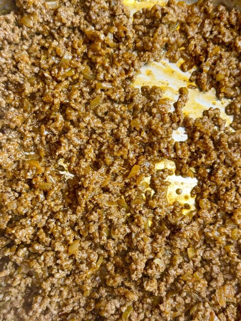 Ground beef cooking with onions, tomato paste, and spices in a pan, simmering into a flavorful taco filling.