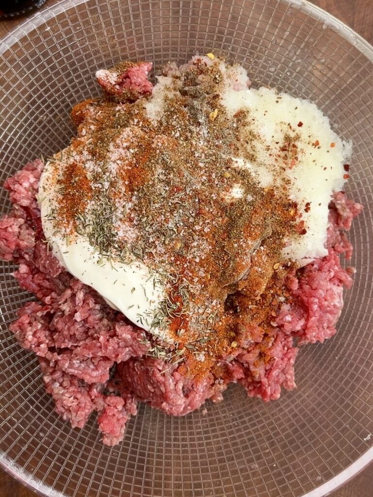 Ground beef in a large bowl mixed with onion–garlic paste, yogurt, and spices