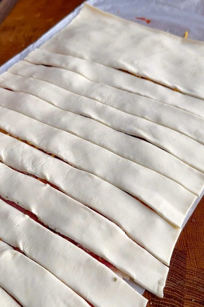 Puff pastry sheet being cut into 15 even strips using a sharp knife or pizza cutter.