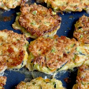 Zucchini patties frying in a pan with a golden, crispy exterior.